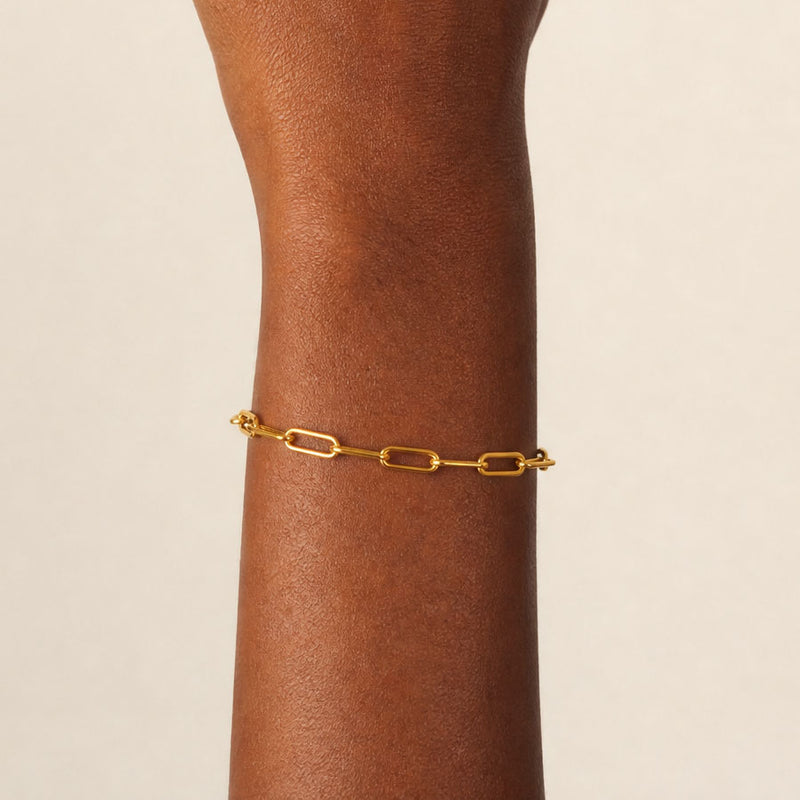 Gold paperclip link bracelet on a person's wrist against a beige background