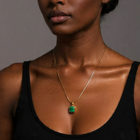 Woman wearing a gold necklace with a green pendant against a gray background