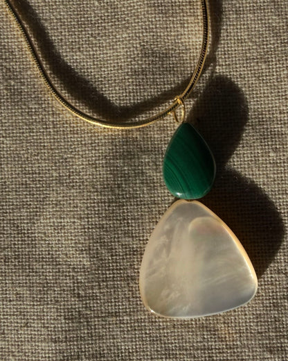 gold snake chain herringbone necklace with a malachite mother of pearl pendant Necklace with a green and white pendant on a textured fabric background