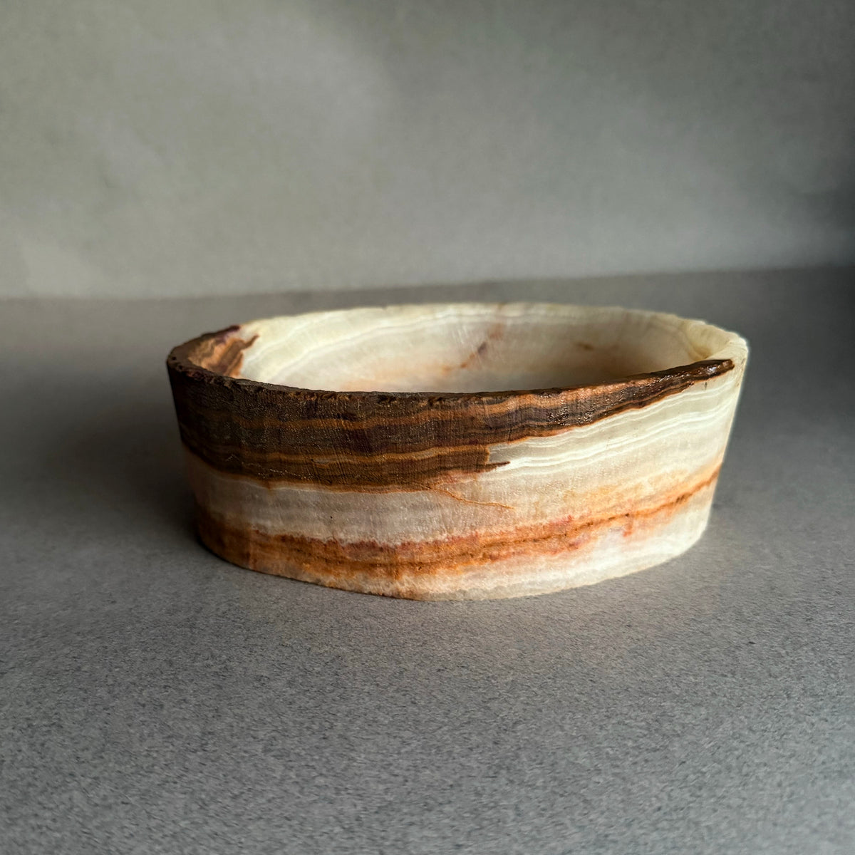 Hand carved white and brown onyx catchall bowl with natural layered stone banding on gray background
