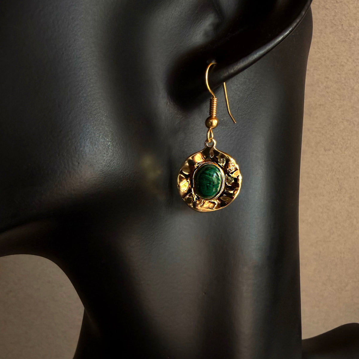 Handmade malachite gold medallion dangle earring worn on black sculptural bust, featuring deep green stone and hammered gold finish
