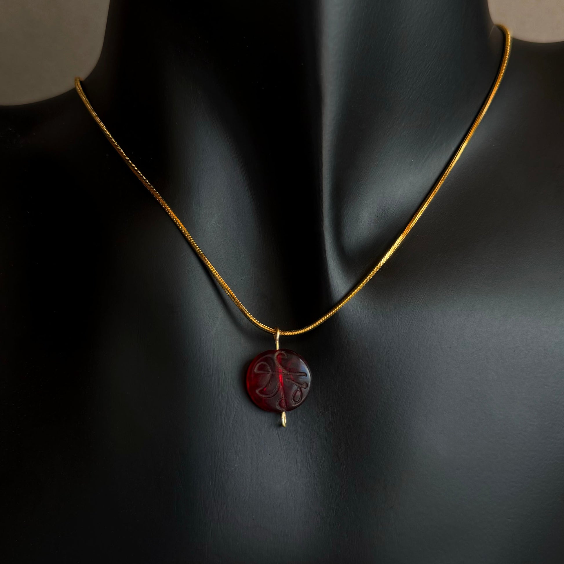 Necklace with a red pendant on a black mannequin Red garnet engraved pendant necklace on gold waterproof snake chain displayed on black bust
