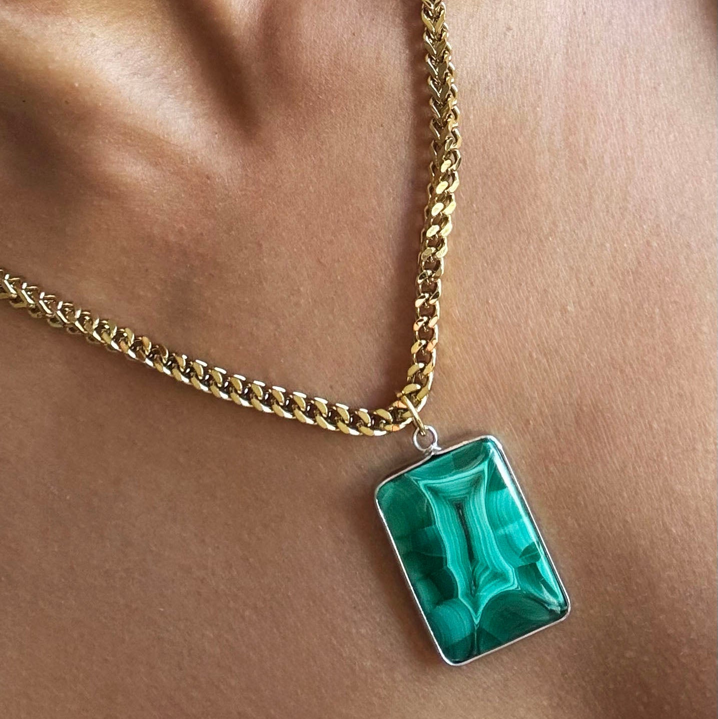 Gold chain necklace with a green rectangle malachite pendant on a beige background