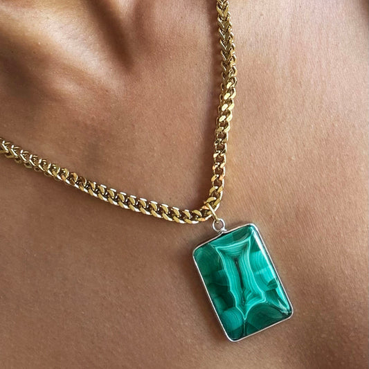 Gold chain necklace with a green rectangle malachite pendant on a beige background