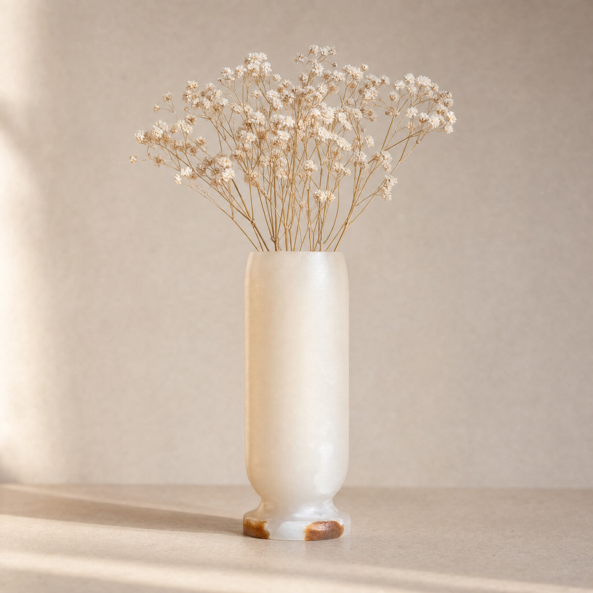 White onyx vase with dried flowers on a neutral background