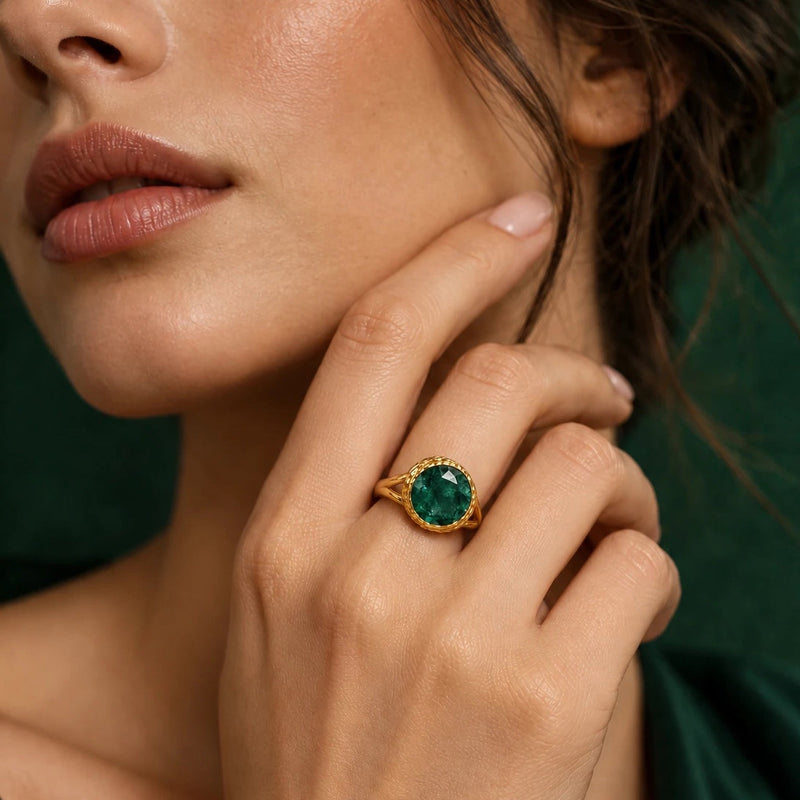 Deep green faceted stone ring worn on a hand resting at the jaw, the round stone in a hammered 22k gold-filled bezel, against dark green velvet