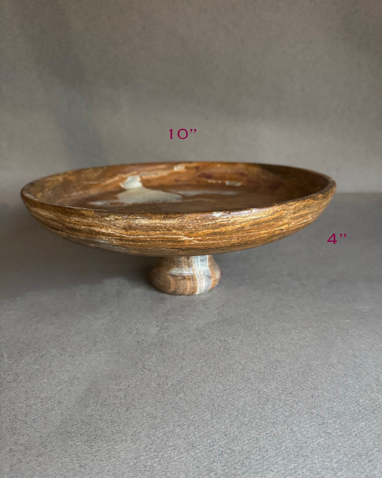 Angled view of cream and honey onyx pedestal bowl, sculptural stone decor piece for dining table, kitchen island, or jewelry catchall.
