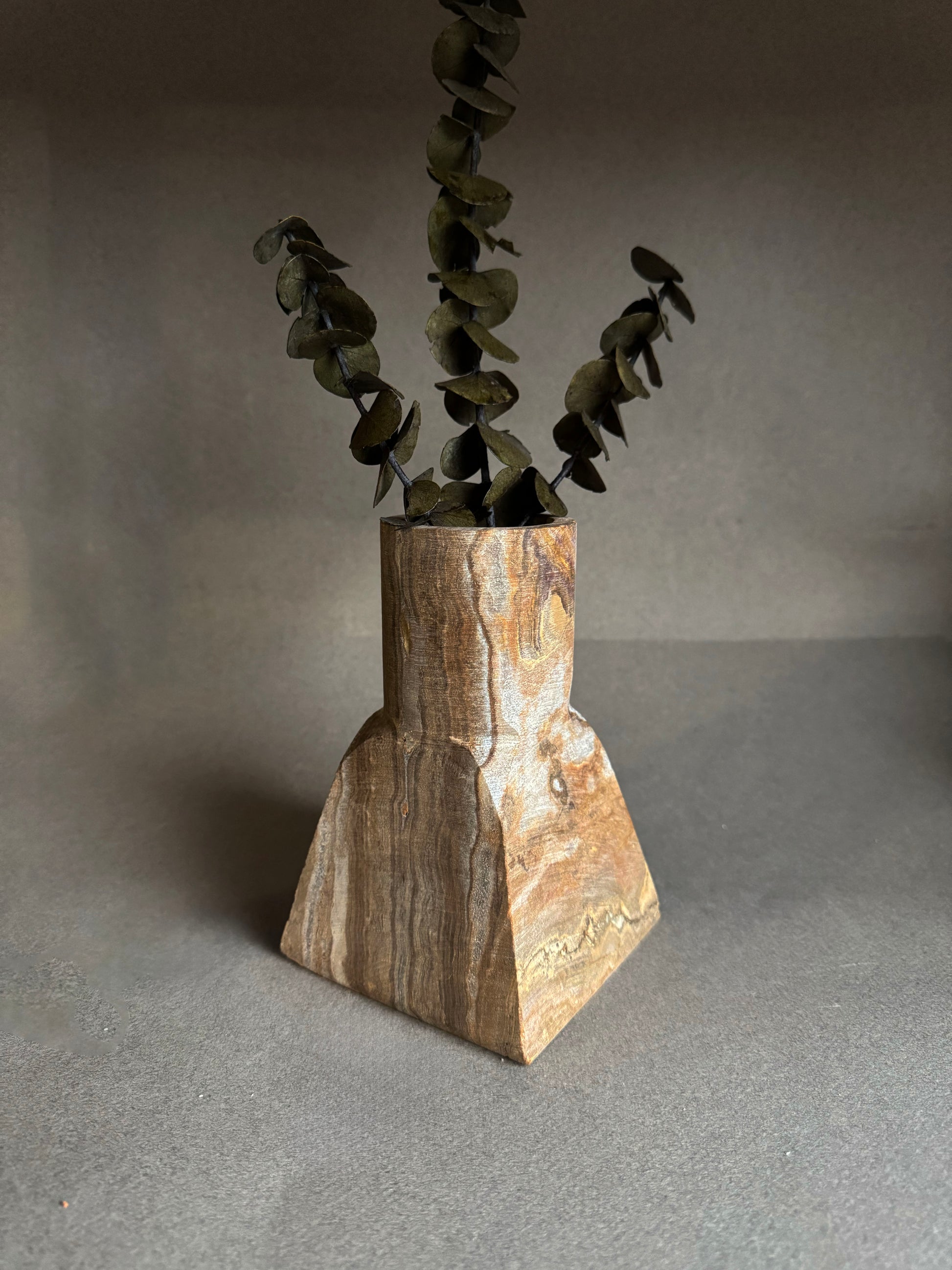 Onyx stone vase with a natural finish holding dried leaves on a gray background