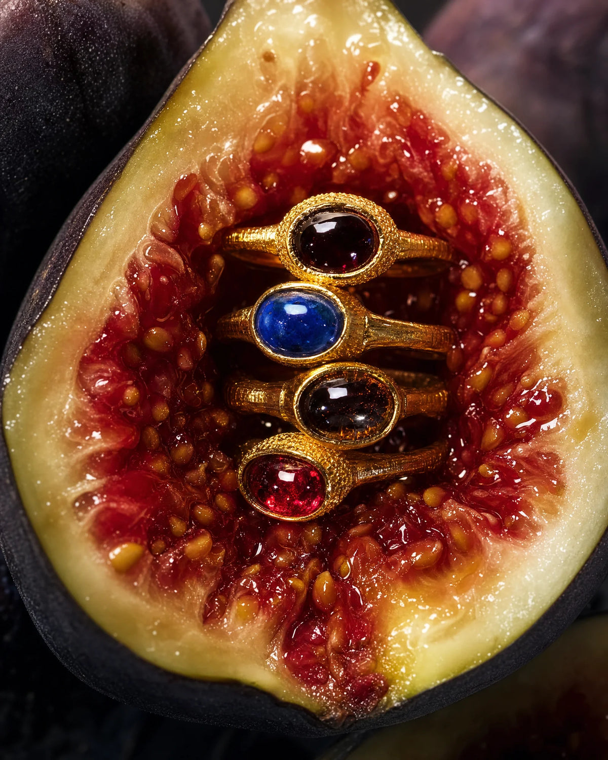 Four gold-plated cabochon rings arranged together, showing the deep red, blood red, midnight blue and tiger's eye quartz stones in granulated bezel settings.
