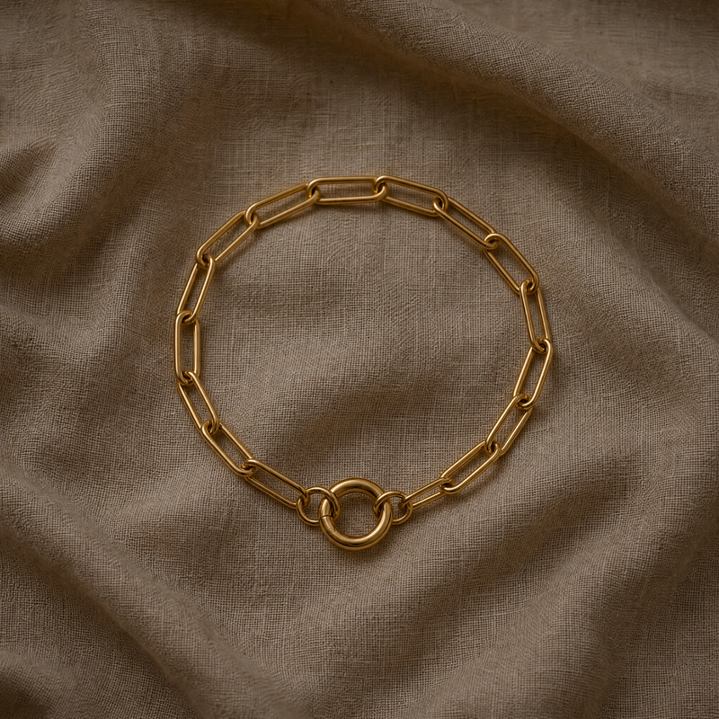 Gold paperclip chain bracelet laid flat on linen, showing elongated links and round push-gate clasp

