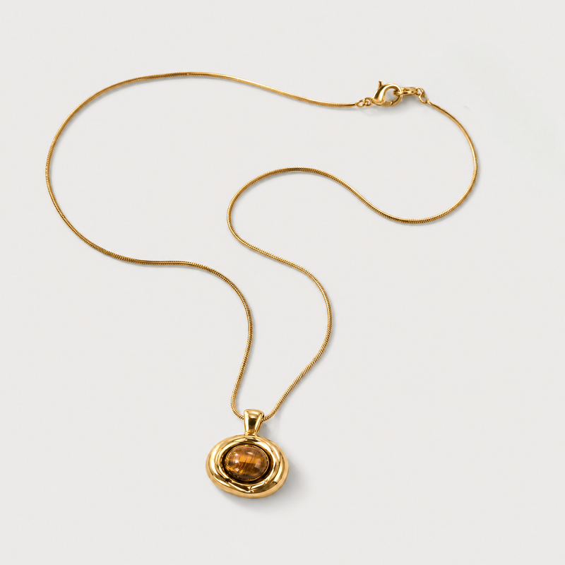 Gold snake chain necklace with a tiger's eye brown stone pendant on a light gray background