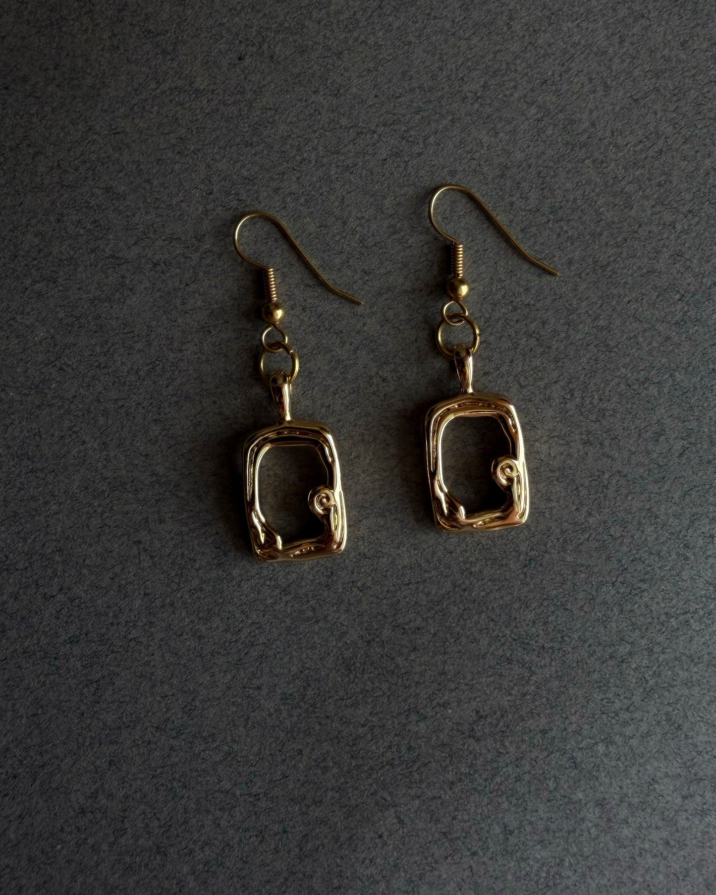 Pair of gold earrings on a dark gray background Close up of gold sculptural drop earring with organic open frame design, handmade 14k gold filled jewelry
