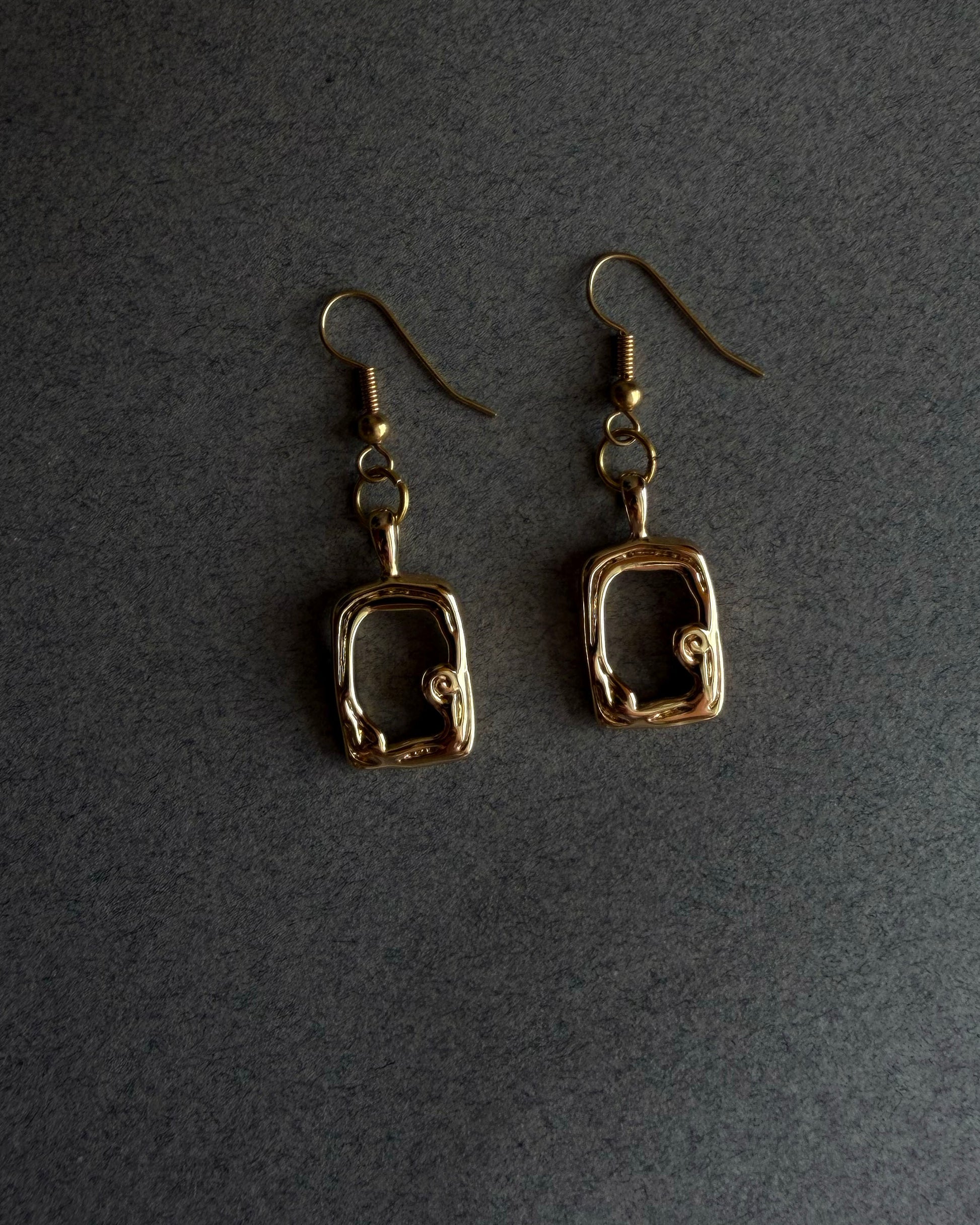 Pair of gold earrings on a dark gray background Close up of gold sculptural drop earring with organic open frame design, handmade 14k gold filled jewelry
