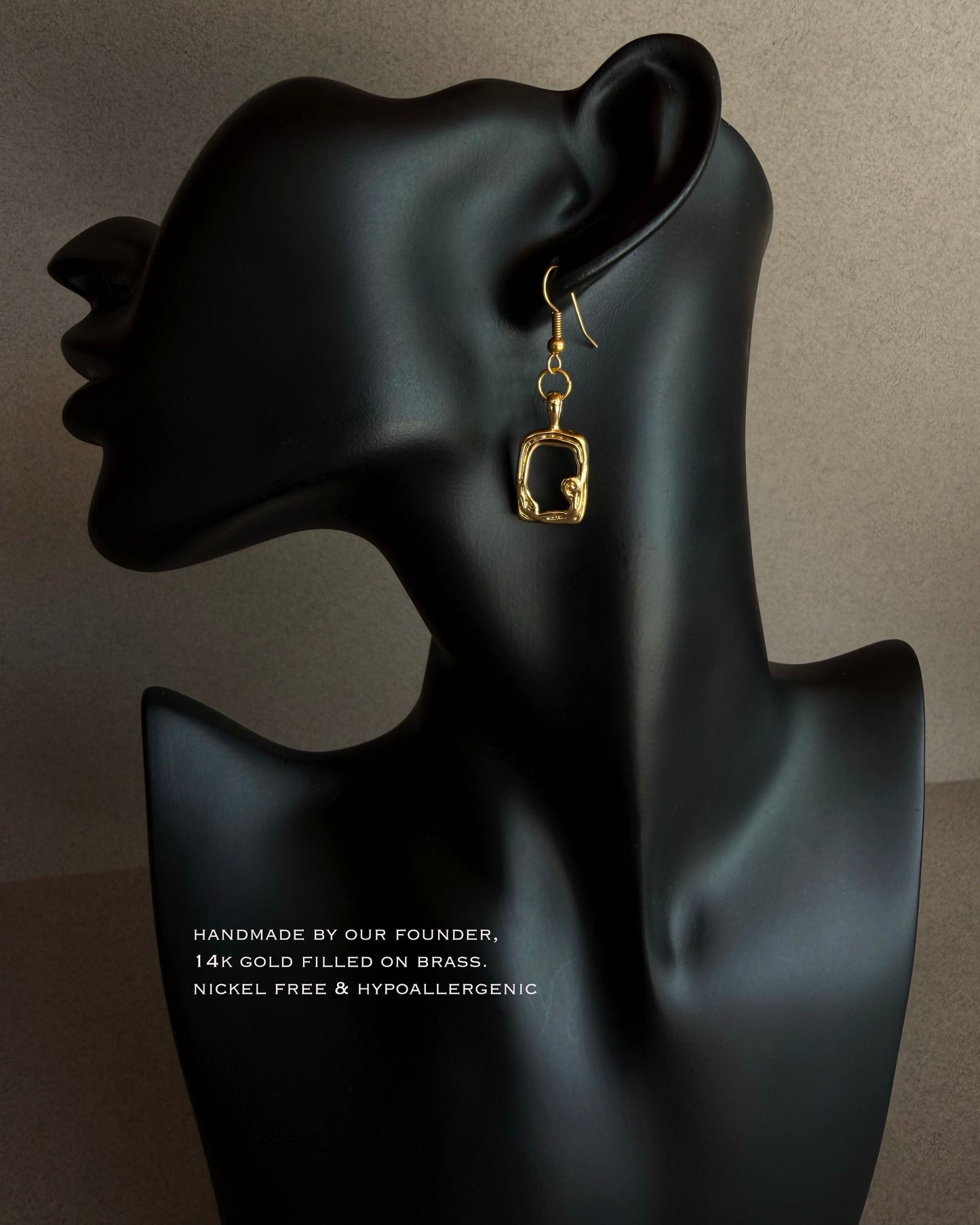 Gold earring on a black mannequin ear with product details text. Modern gold sculptural earrings worn on black bust, lightweight waterproof statement earrings, minimalist gold jewelry
