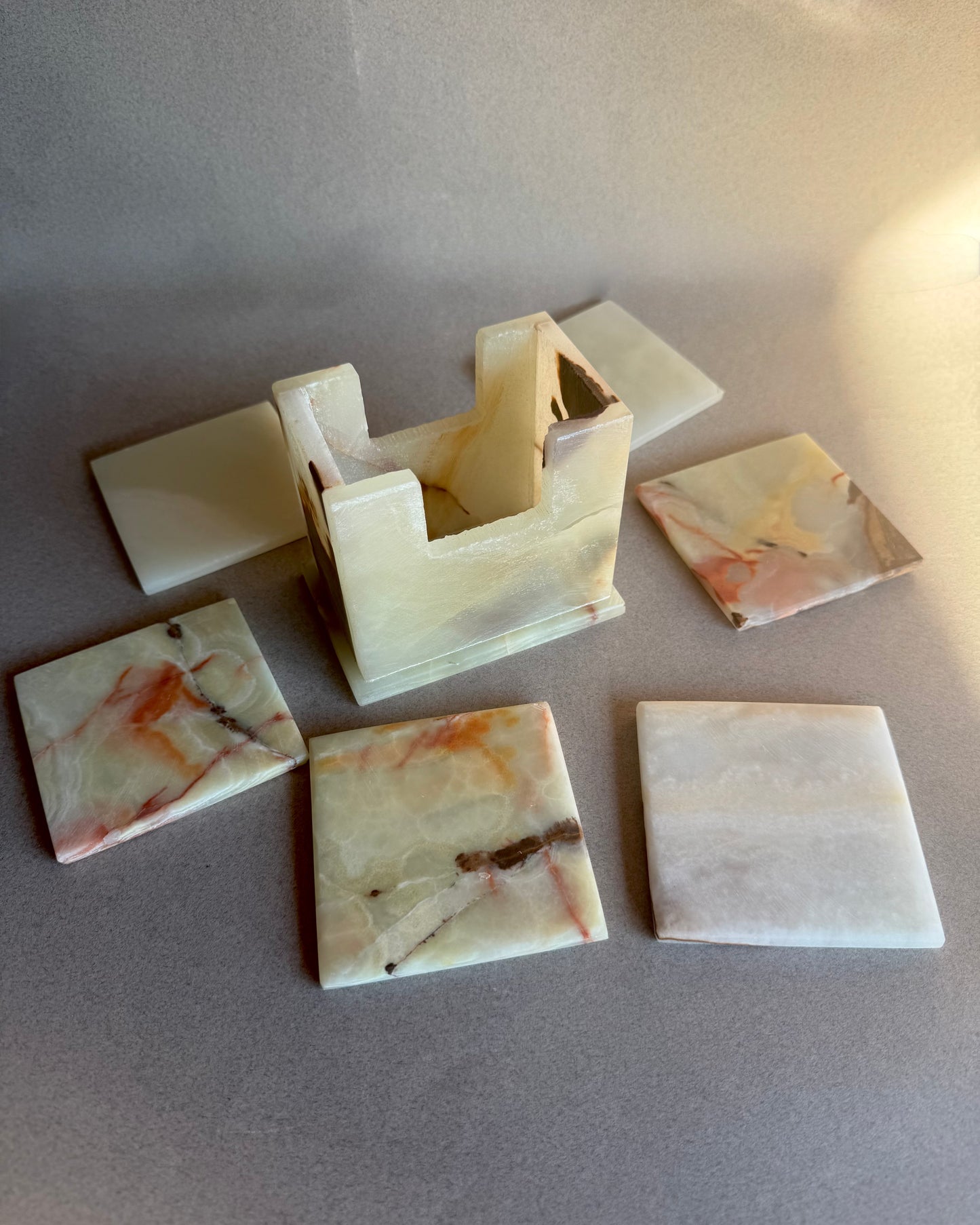 Hand-carved stone coaster holder in ivory and beige onyx with subtle rust marbling, square sculptural design.