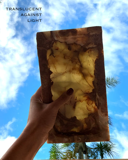 Hand holding a translucent onyx stone catcall tray  against a blue sky with clouds