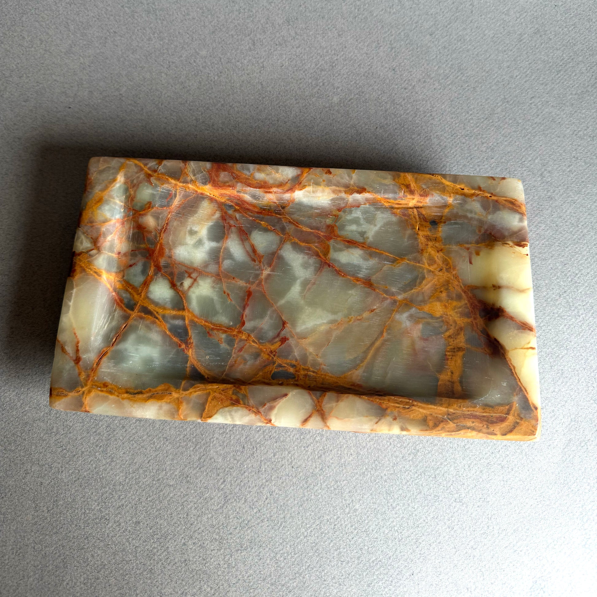 Marble-like onyx stone catchall tray with brown and beige patterns on a gray background