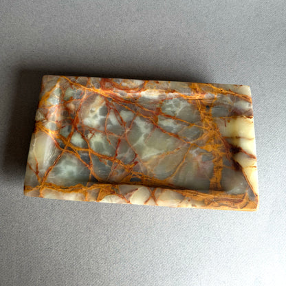 Marble-like onyx stone catchall tray with brown and beige patterns on a gray background