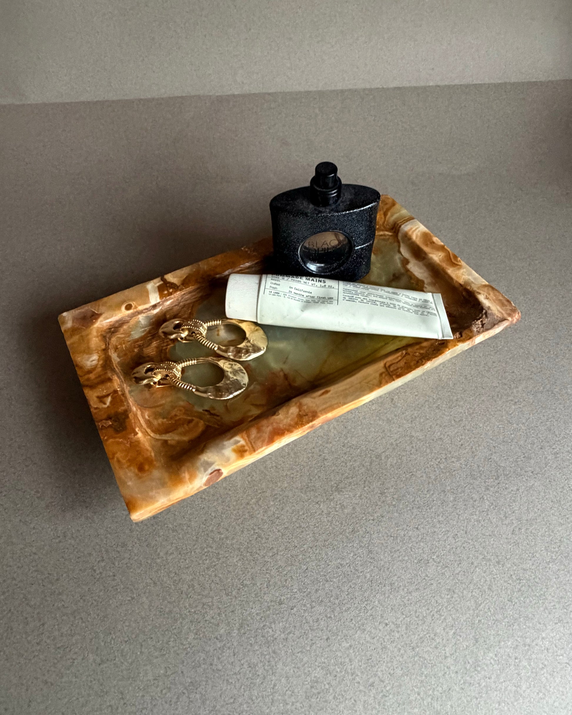 Decorative stone onyx catchall tray with jewelry and a small black container on a gray surface