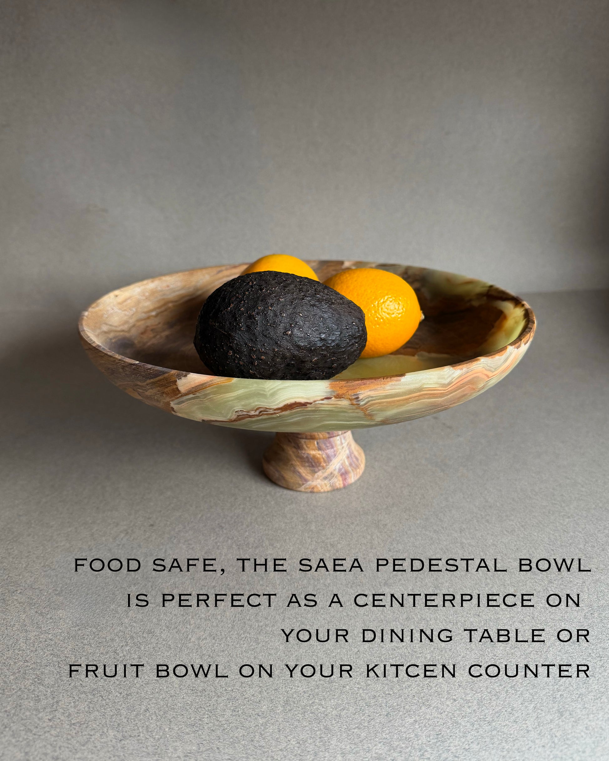 Decorative pedestal bowl with fruit on a gray surface, featuring text about its use.