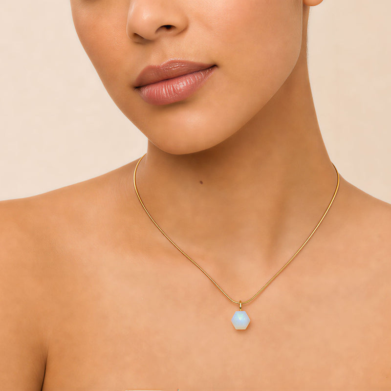 Model wearing SAÉA opalite hexagon pendant necklace on 18-inch 14k gold-filled snake chain against warm peach background
