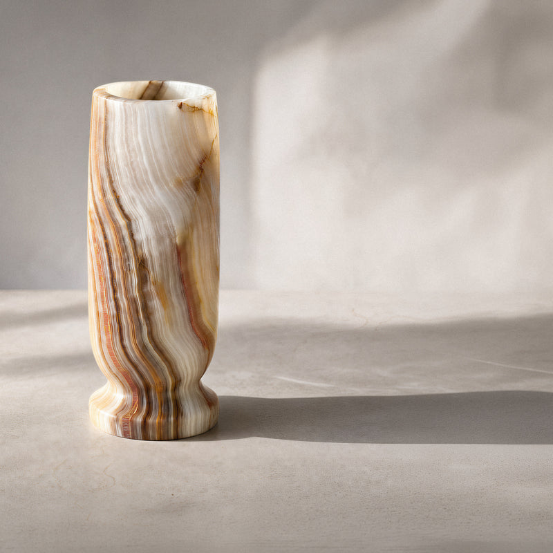 Tall slender onyx vase holding white dried baby's breath in warm window light on a wood table.
