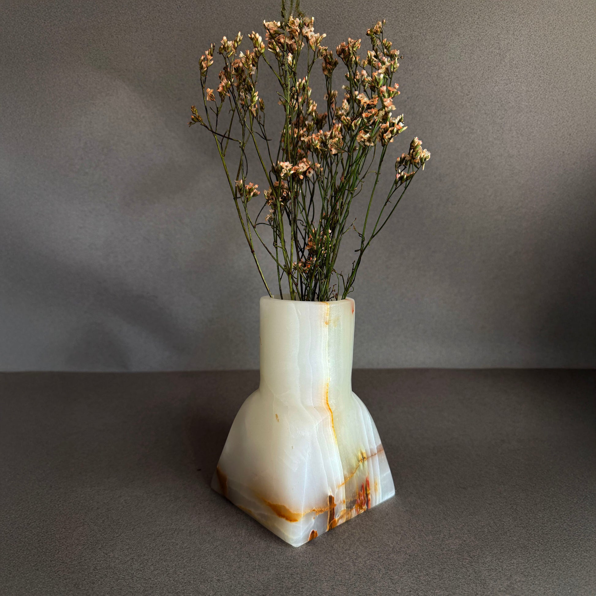Decorative white onyx vase with dried flowers on a gray background