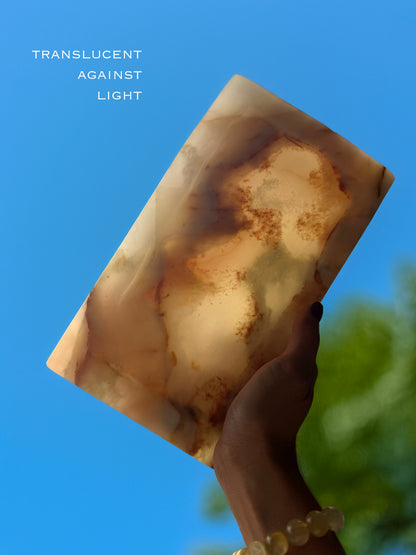 Hand holding a translucent onyx tray against a blue sky with trees in the background.
