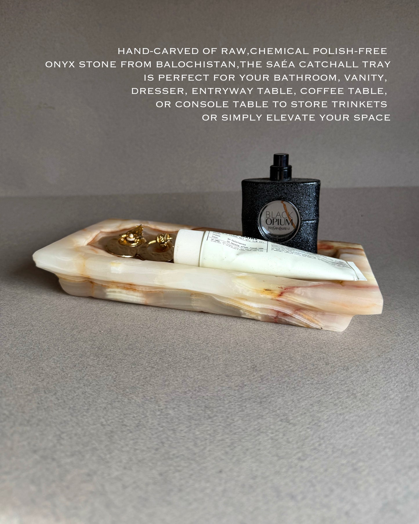 Onyx stone catchall tray with a bottle and tube of cream on a gray surface.