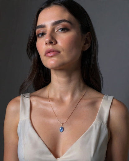 Woman wearing a snake chain necklace with a blue pendant against a neutral background