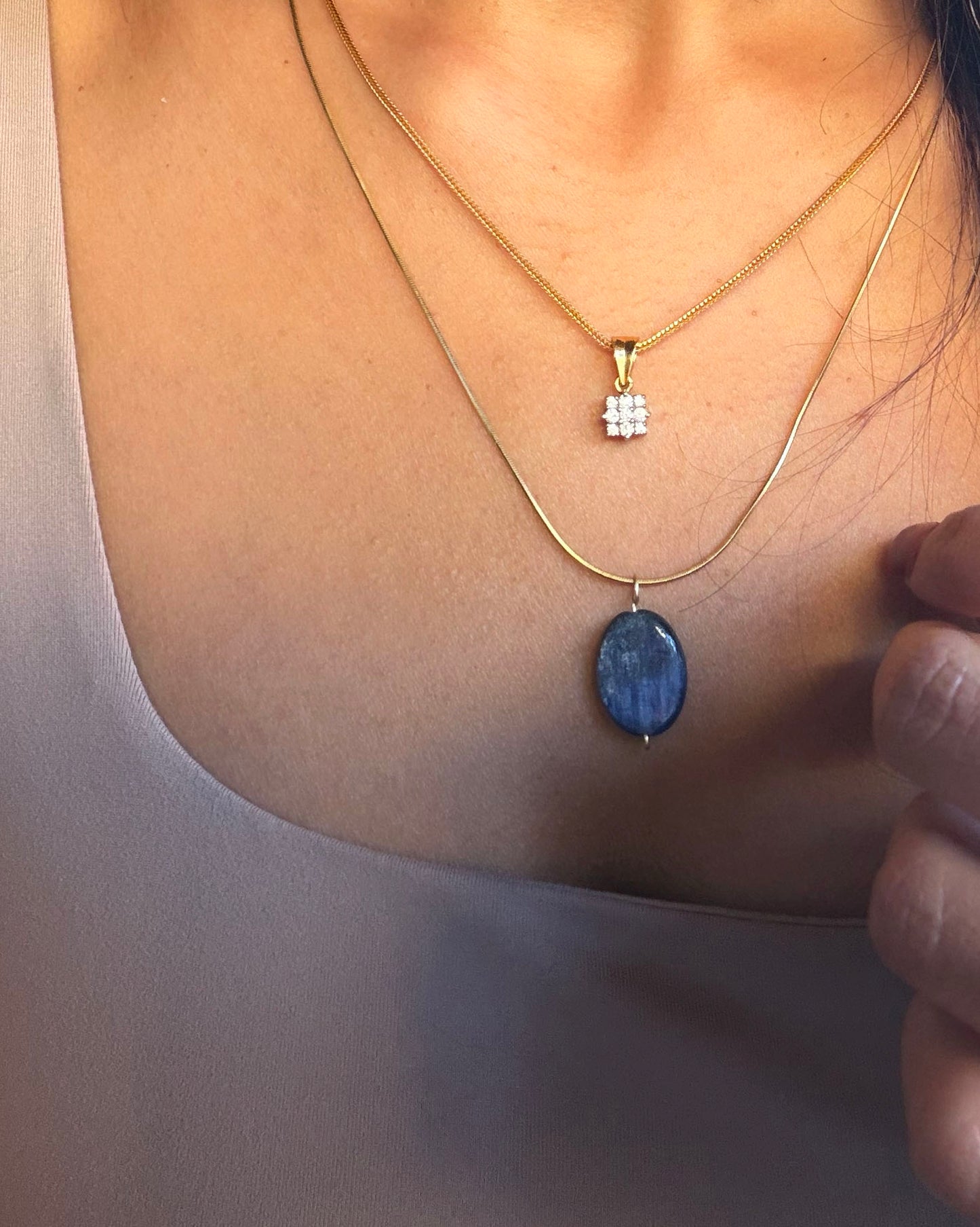Two necklaces with blue stone pendants on a person's neck against a neutral background