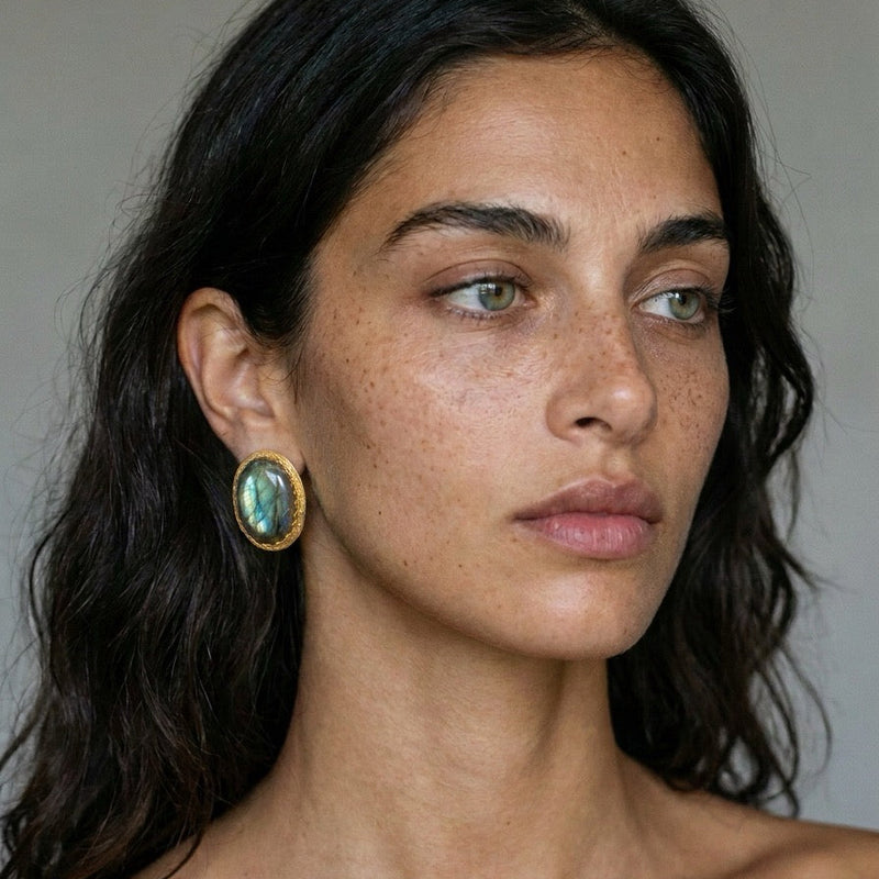 Model wearing an oval labradorite statement stud in 22k gold plate, against a gray background