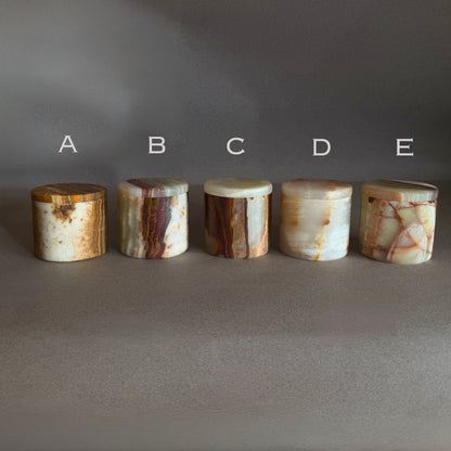 Five cylindrical onyx stone jars with lids salt jars labeled A to E on a gray background