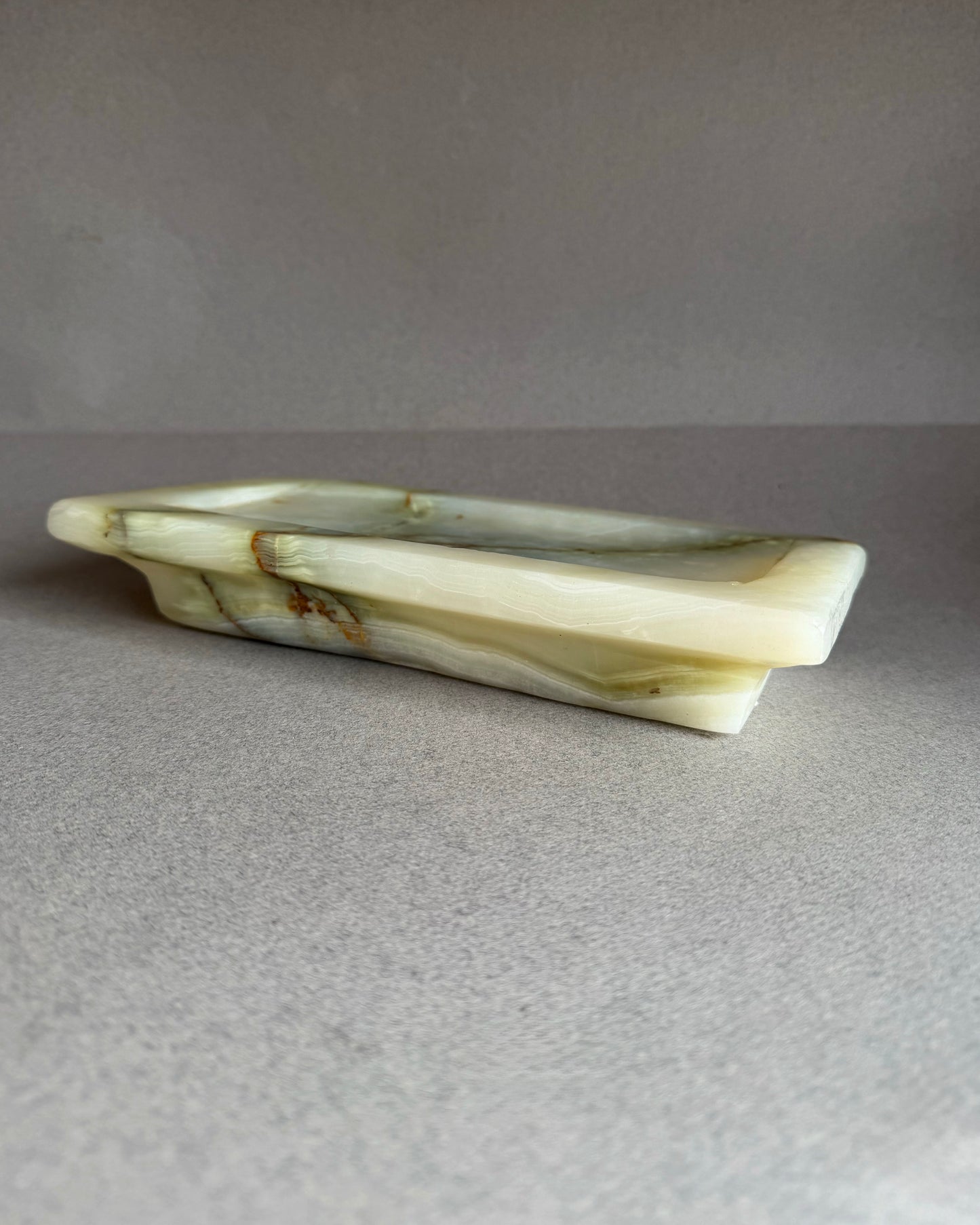 White green onyx stone catchall tray with green veins on a gray background