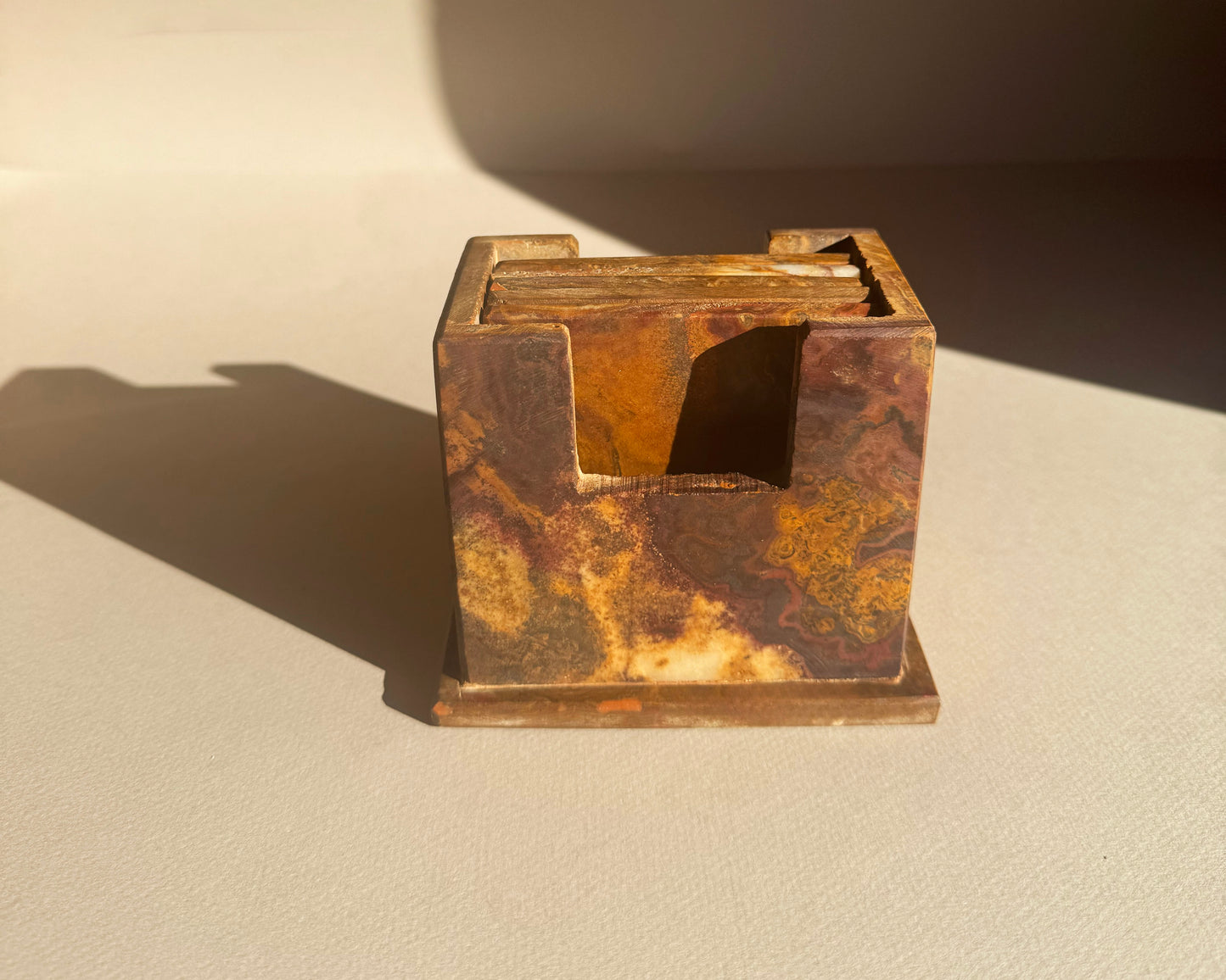 Rust-colored square coaster holder set on a beige surface