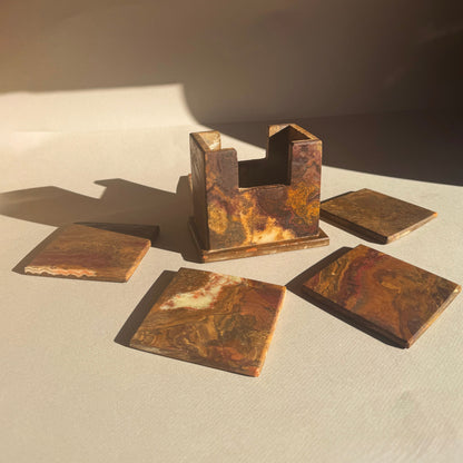Rust-colored stone coaster holder and square coasters on a light surface with a dark background