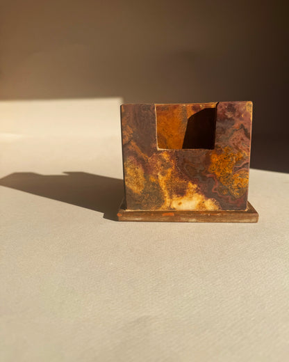 Rust-colored coaster holder made of onyx marble stone on a beige surface with a brown background