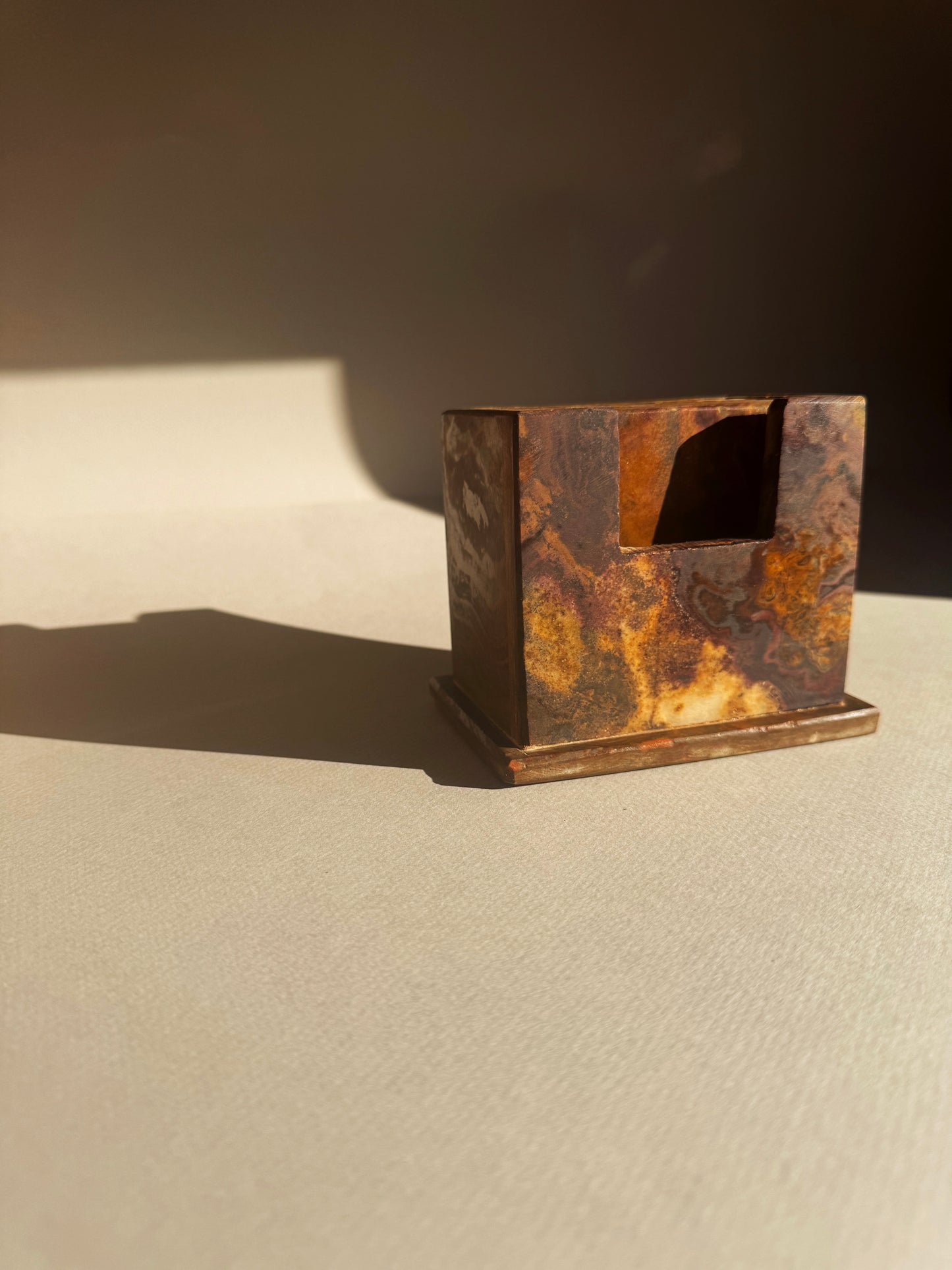 Rust-colored coaster holder and coasters on a beige surface with a dark background