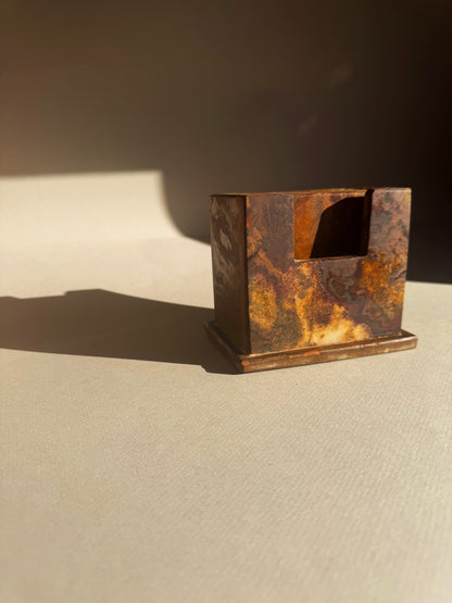 Rust-colored coaster holder and coasters on a beige surface with a dark background
