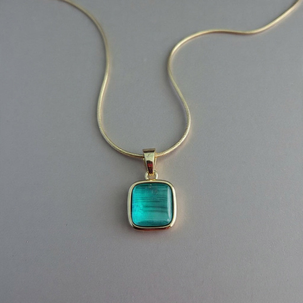 Gold necklace with a green pendant on a gray background
