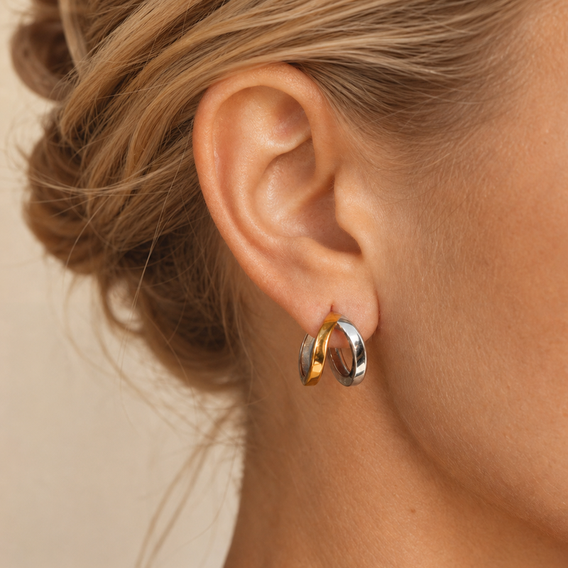 Close-up of an ear wearing gold and silver mixed metal hoop earrings on a neutral background