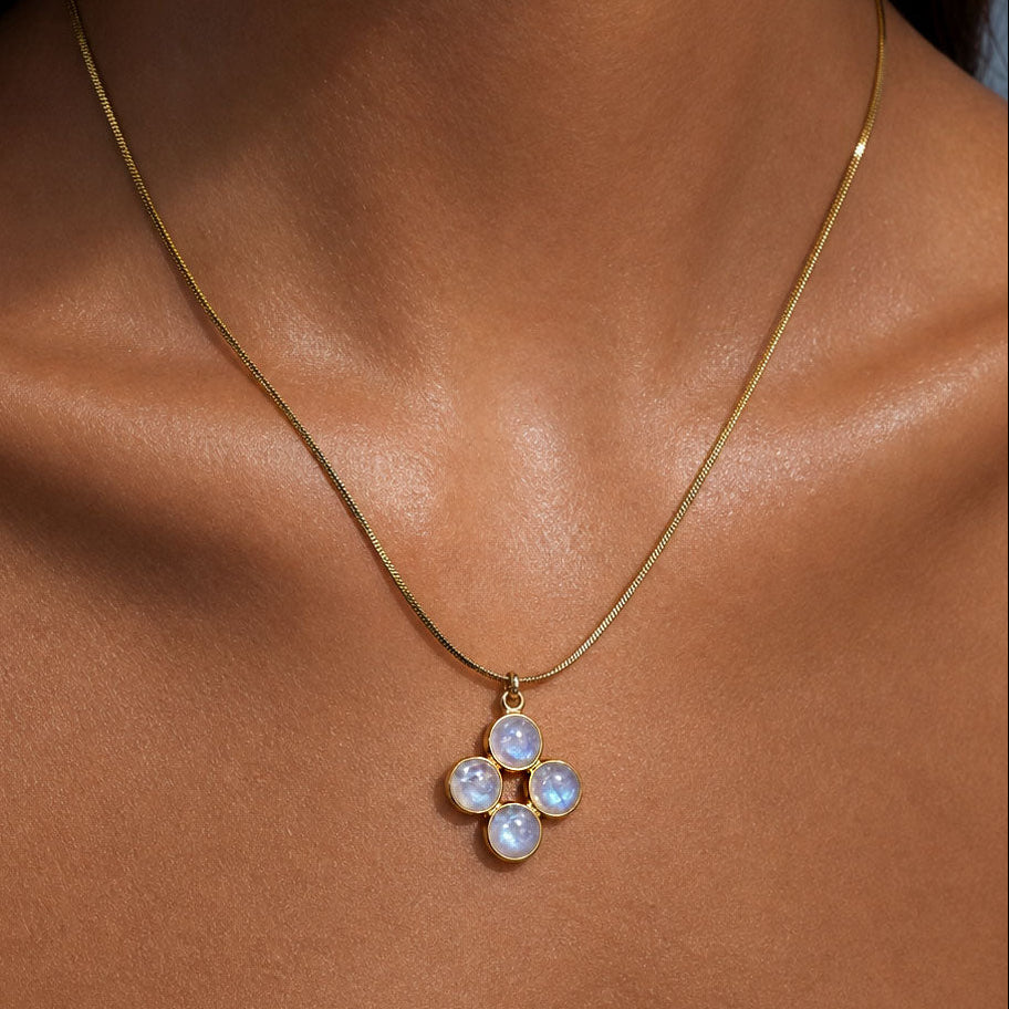 Close-up of the four-petal rainbow moonstone pendant resting at the collarbone on a gold snake chain, blue flash visible in the stones.