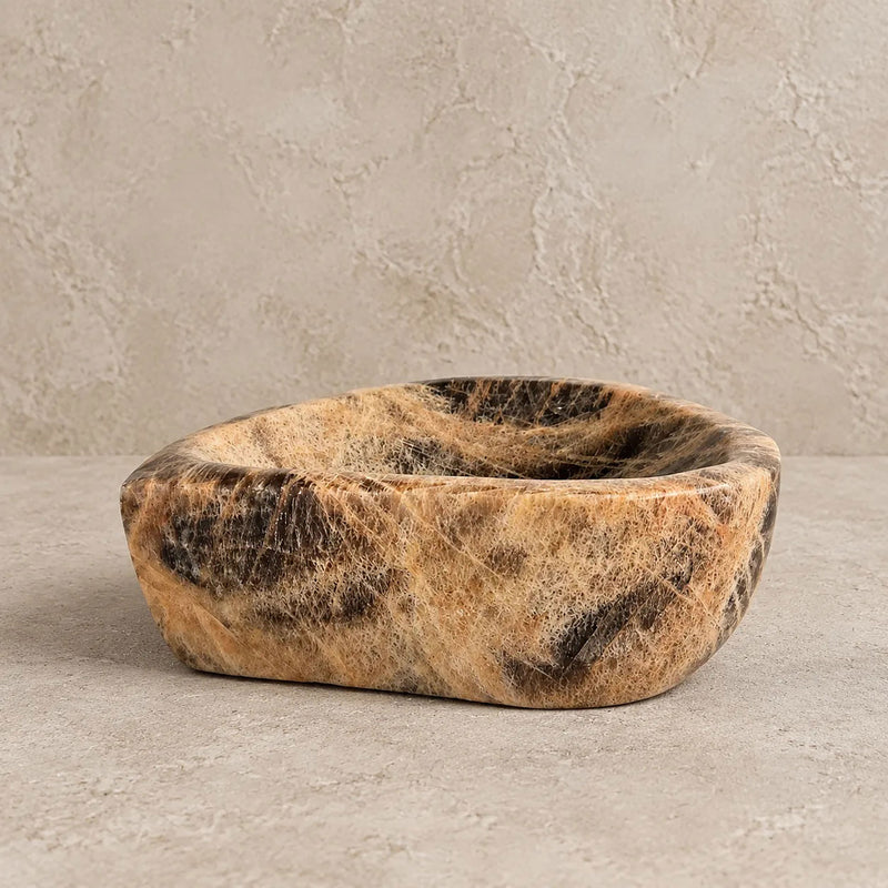 Front view of the black moonstone pebble catchall, fine fibrous lines running through peach and sand