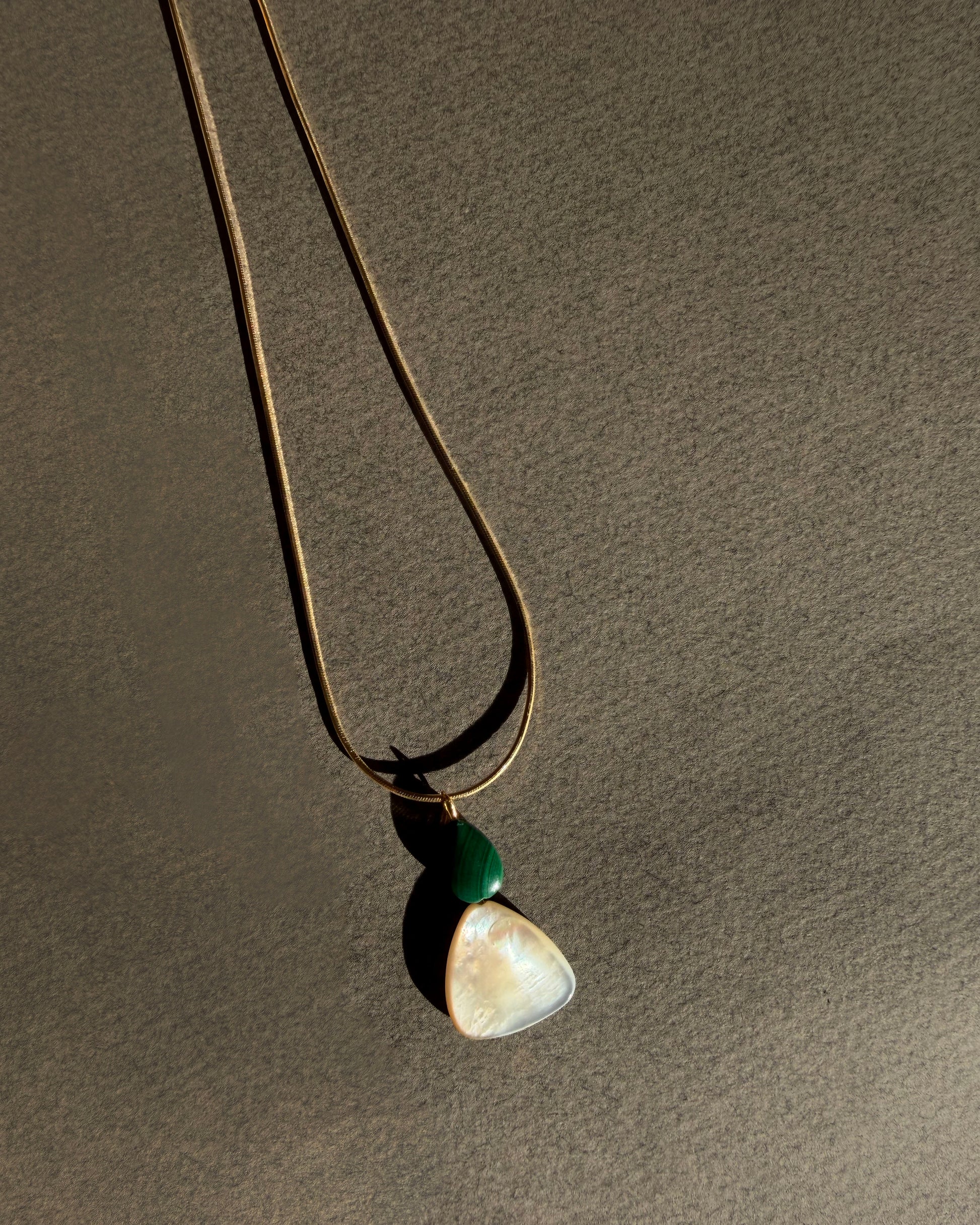 gold snake chain herringbone necklace with a malachite mother of pearl pendant Necklace with a pendant on a brown background