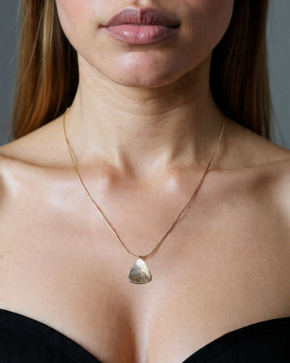 gold snake chain necklace with a pendant worn by a person, focusing on the necklace and iridescent mother of pearl