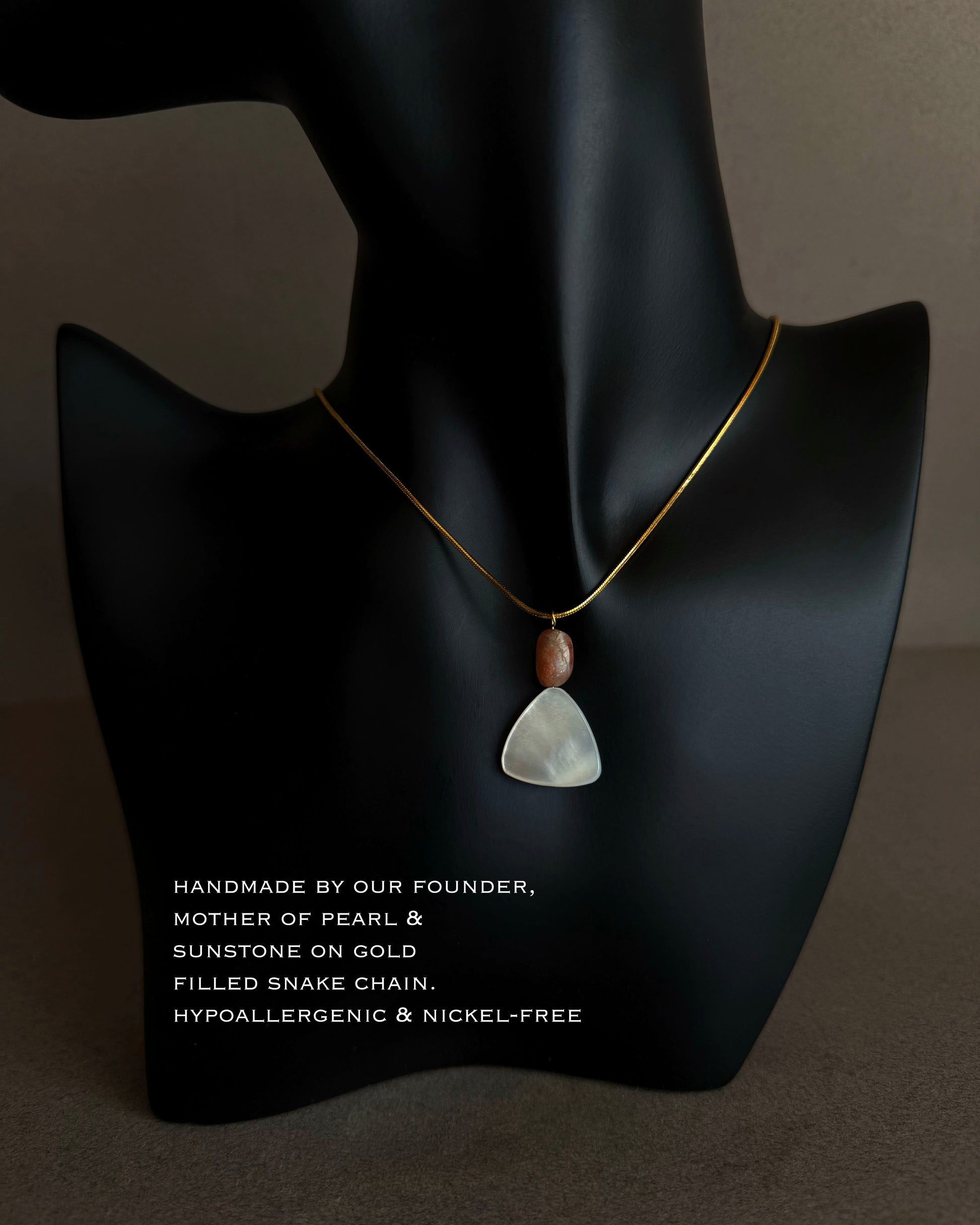 Close-up of mother of pearl pendant showing natural iridescence and soft triangular shape
 Necklace with a pendant on a black mannequin bust against a dark background