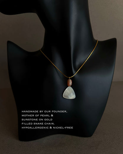 Close-up of mother of pearl pendant showing natural iridescence and soft triangular shape
 Necklace with a pendant on a black mannequin bust against a dark background