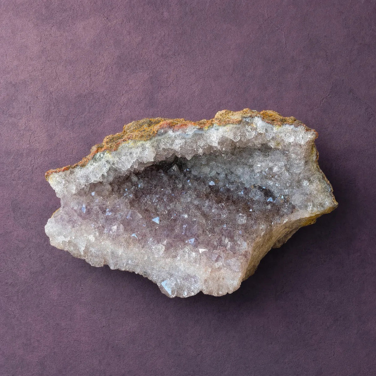 Natural amethyst geode standing upright, ochre matrix rind on the outside with a band of pale crystal along the base.