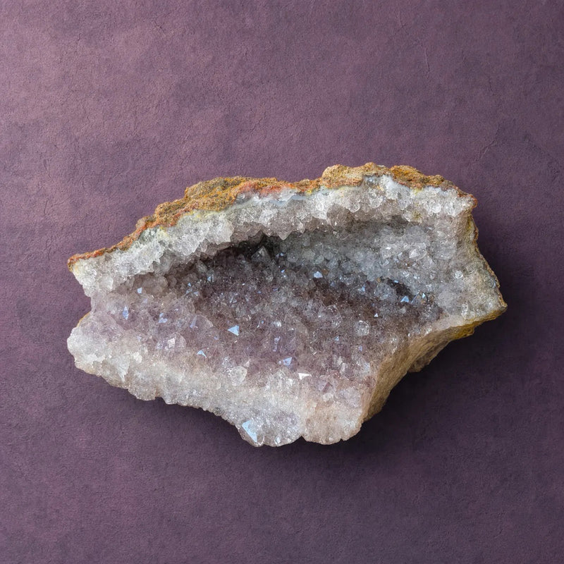 Natural amethyst geode standing upright, ochre matrix rind on the outside with a band of pale crystal along the base.