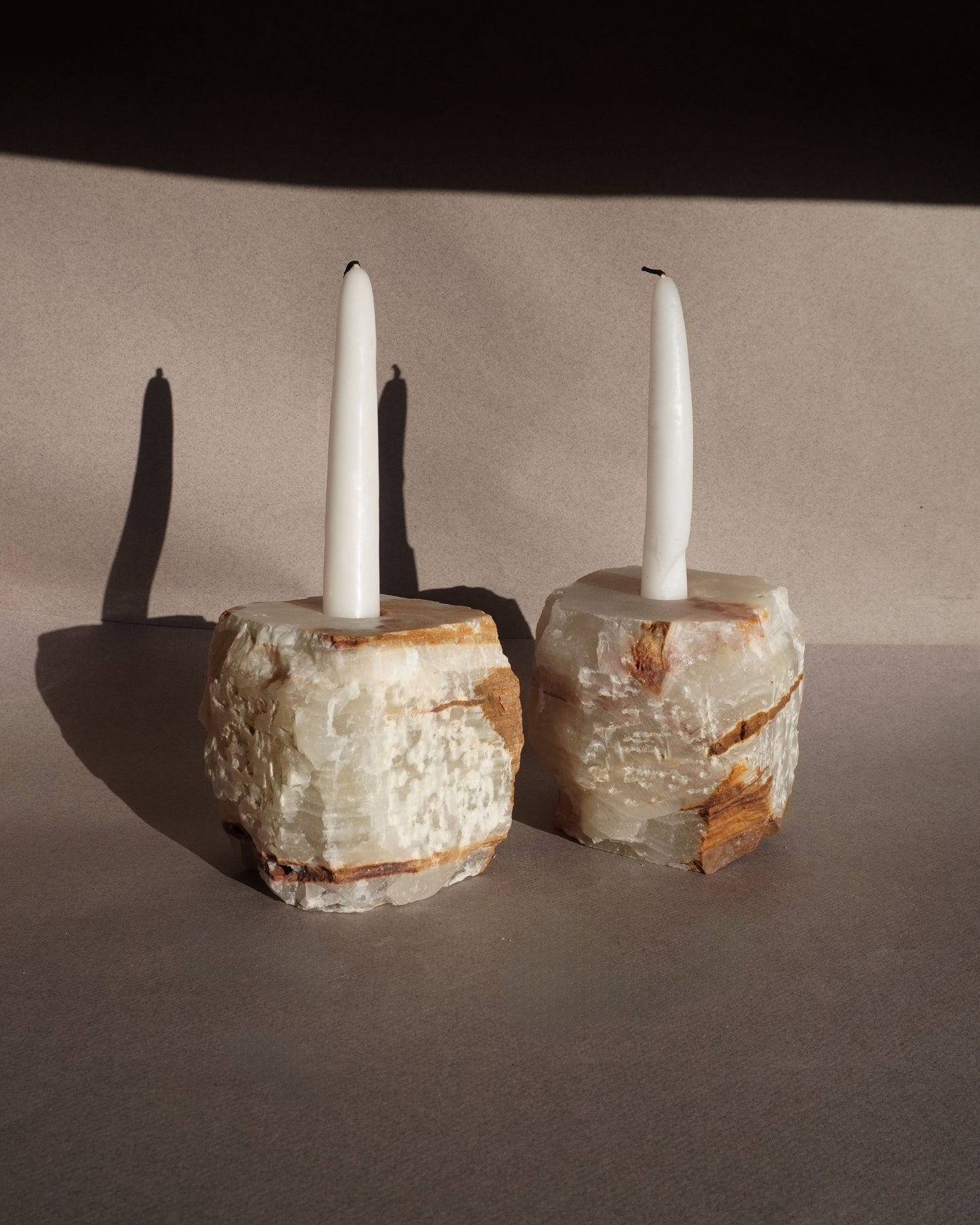 Two candle holders made of textured stone material with candles on a neutral background Minimalist stone taper candle holders made from solid onyx with organic texture and visible mineral layers
